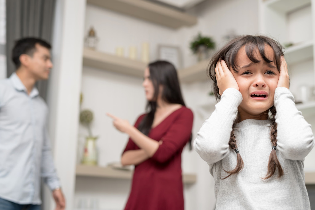 child crying with her parents fighting in the back